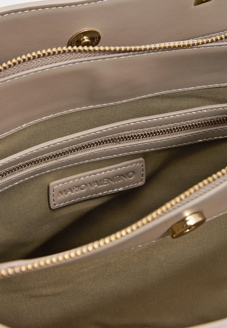 Intérieur de sac à main beige avec plusieurs compartiments zippés, texture en cuir lisse et quincaillerie en ton doré. Étiquette visible : "MARIO VALENTINO."