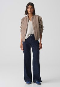 Giubbotto bomber khaki, top bianco a coste, jeans a gamba larga blu scuro, sneakers blu. Tessuto liscio con dettagli testurizzati ai polsini e al colletto.