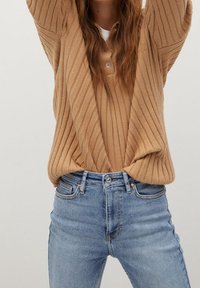 Suéter marrón ribeteado con una botonera, combinado con jeans de tiro alto en azul claro. El suéter presenta un corte holgado y un tejido texturizado.