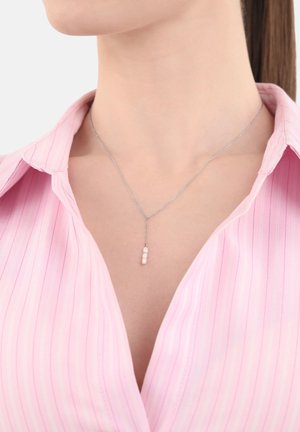 Collana di catena argentata con tre perle rosa, appese verticalmente, indossata con una camicia a righe rosa chiaro.
