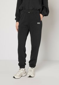 Svarta sweatpants med ribbat mönster och elastisk midja, med sidofickor och en liten logotyp på vänster ben. Kombinerat med vita sneakers.