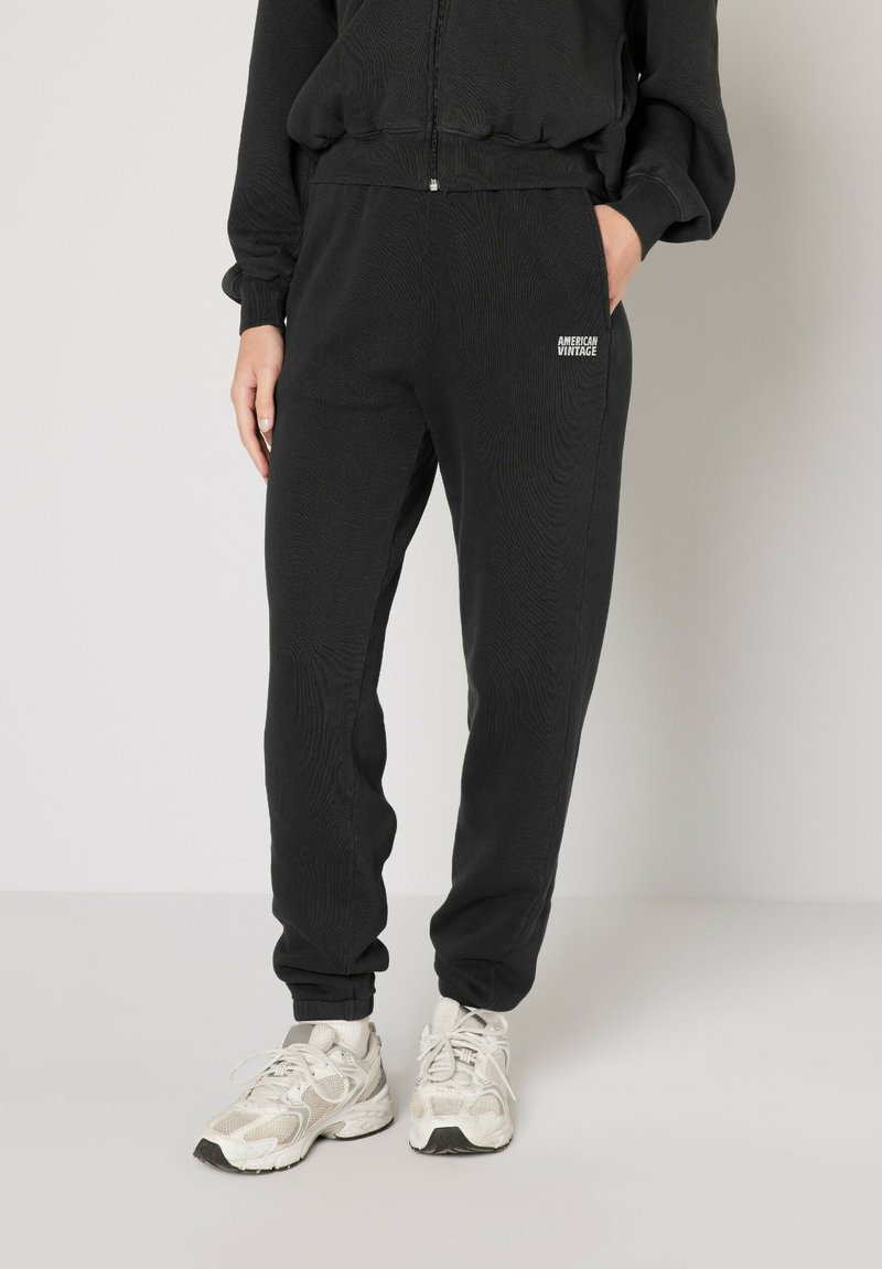 Svarta sweatpants med ribbat mönster och elastisk midja, med sidofickor och en liten logotyp på vänster ben. Kombinerat med vita sneakers.