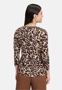 Top con stampa leopardata, maniche a tre quarti, realizzato in un morbido tessuto nei colori marrone, sabbia e nero. Presenta un collo rotondo e una vestibilità comoda.
