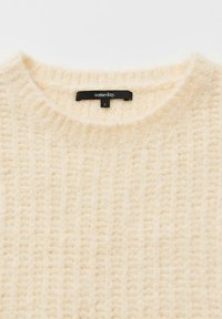 Cremefarbener Strickpullover mit strukturiertem Muster, rundem Ausschnitt und einem schwarzen Etikett mit der Aufschrift "someday." sowie der Größe "S."