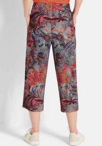 Pantalons courts imprimés multicolores avec des motifs floraux et abstraits ; taille élastique ; tissu doux ; associés à des baskets de couleur claire.