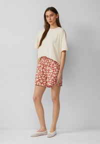 Cremefarbenes, oversized T-Shirt mit lockerer Passform, kombiniert mit korallenrosa Shorts im gepunkteten Muster. Leichtes, atmungsaktives Material; flache, weiße Schuhe.