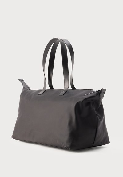 Μαύρη ορθογώνια μαλακή δερμάτινη τσάντα tote με διπλές λαβές και φερμουάρ στο πάνω μέρος, παρουσιασμένη σε απλό ανοιχτό φόντο.