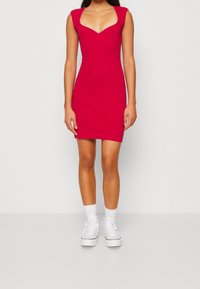 Aansluitend, mouwloze rode jurk met een V-hals, gemaakt van een zachte stof. Gepaard met witte sneakers en enkelsokken.