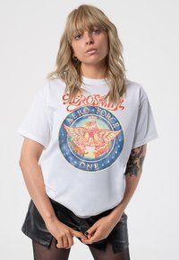 White cotton t-shirt featuring a colorful graphic design with a stylized eagle, text "Aerosmith Aeroforce One," and round blue accents.