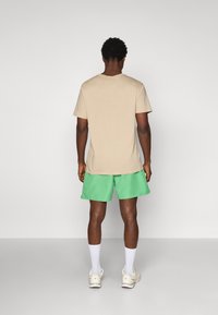 Tricou din bumbac bej, cu guler tip crew, asortat cu pantaloni scurți verzi. Pantalonii scurți au un brâu elastic și o textură ușoară, netedă.