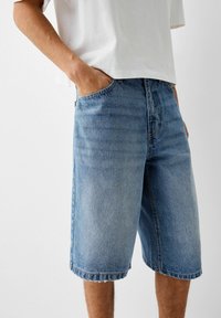 Jeansshorts i ljusblått, med en avslappnad passform, fem fickor och fransad fåll. Bärs med en löst sittande vit t-shirt.