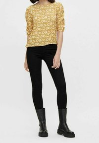 Haut jaune à motifs avec manches aux trois quarts, associé à un jean noir ajusté et des bottines noires à semelle épaisse.