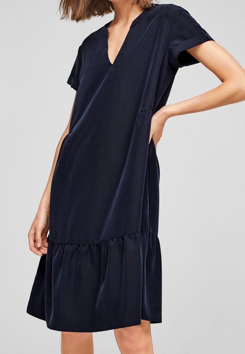 Femme portant une robe ample à manches courtes bleu marine avec un col en V et un ourlet à volants froncés.