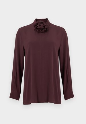Burgunderrød bluse med lange ermer og høy hals, med en fremtredende blomsterdetalj på kragen laget av glatt stoff.