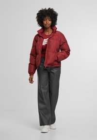 Rode pufferjack met een zigzagpatroon, hoge kraag en voorzakken, gecombineerd met een donkergrijze outfit en witte sneakers.