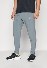 Vaaleanharmaat Nike-juoksuhousut, joissa on kapeampi malli, joustava vyötärö, sivutaskut ja vetoketjut nilkassa. Yhdistetty mustiin lenkkareihin.