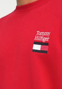 Sweatshirt en coton rouge avec un col rond et un logo brodé présentant un design de drapeau rectangulaire en rouge, blanc et noir.