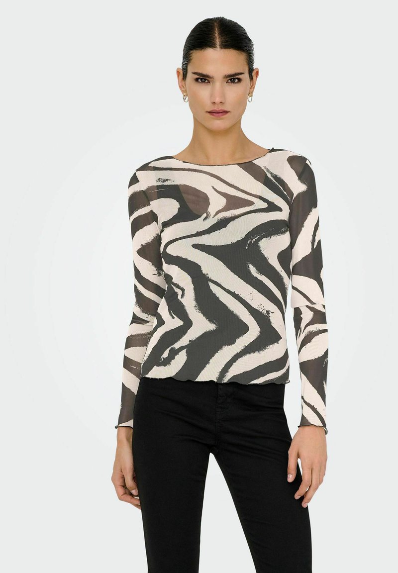 Długo rękawowa, przezroczysta bluzka w falisty czarno-kremowy wzór w zebrę. Okrągły dekolt i dopasowany krój, w połączeniu z czarnymi spodniami.