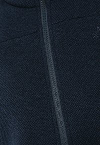 Marineblaues Zip-Jackett aus strukturiertem Strickstoff, mit markantem Reißverschlussdetail und einem dezenten Logo auf der oberen linken Seite.