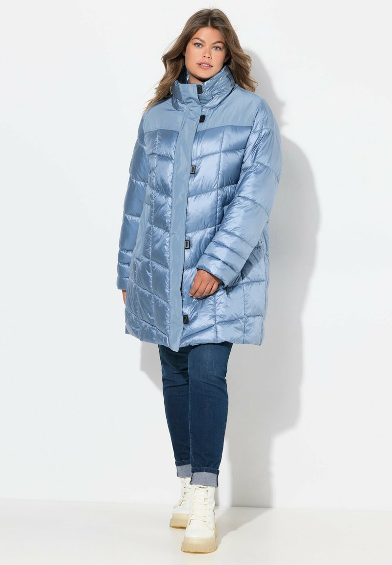 Abrigo acolchado azul claro con cuello alto, diseño acolchado y cierres de botones. La tela parece brillante, con bolsillos laterales.