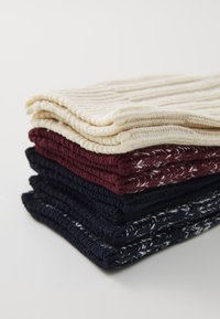 Knit washcloths stacked in cream, burgundy, and navy, featuring textured ribbing and a white accent pattern on the navy cloth.