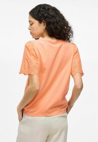 Camiseta de algodón melocotón con mangas cortas abullonadas y ribete de encaje bordado. Cuello redondo sencillo, corte relajado y textura suave.