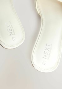 Sandales blanches avec une semelle intérieure rembourrée, une forme arrondie et des bords cousus. Présente un logo sur la semelle intérieure. Texture douce.