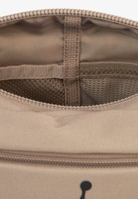 Pochette beige zippée en tissu lisse et texturé, avec une poche en mesh à l'intérieur. Comprend une fermeture éclair robuste et une petite boucle pour attachement.