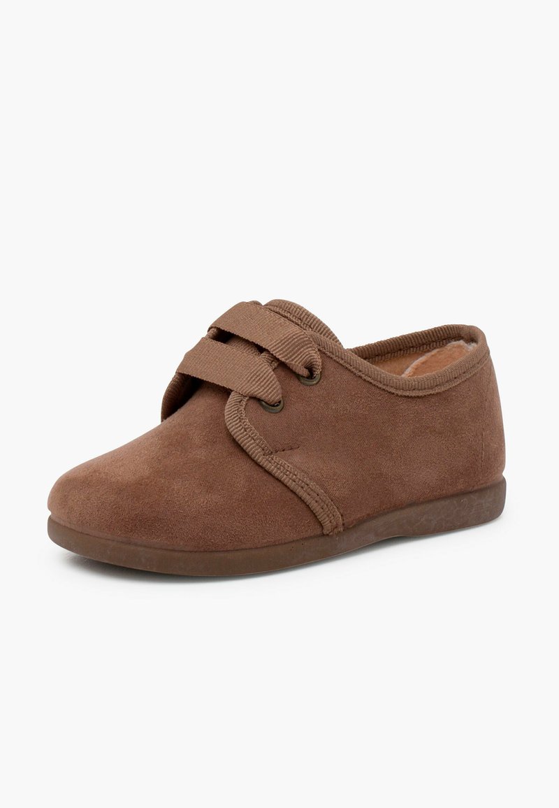 Papuci din suede maro cu vârful rotunjit, curea elastică și căptușeală interioară moale. Talpa din cauciuc cu profil redus oferă aderență.
