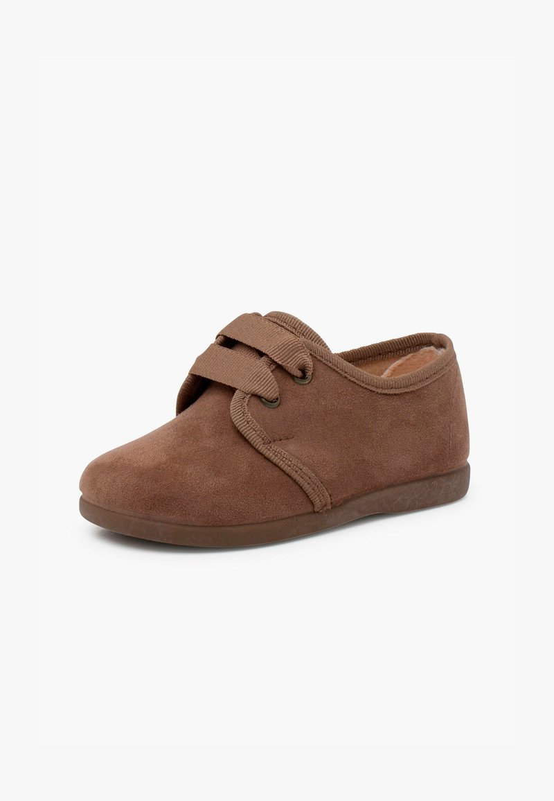 Papuci din suede maro cu vârful rotunjit, curea elastică și căptușeală interioară moale. Talpa din cauciuc cu profil redus oferă aderență.