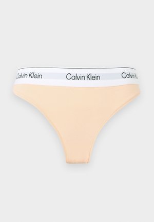 Sous-vêtement beige pour femme, coupe bikini, avec une ceinture élastique blanche ornée de logos Calvin Klein noirs répétés.