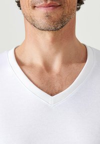 Witte V-hals T-shirt met een zachte textuur, met een subtiele naaddetail bij de halslijn en een relaxte pasvorm rond het kraaggebied.