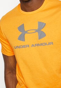 Oranžové bavlněné tričko s šedým logem "Under Armour" na hrudi, klasickým kulatým výstřihem a krátkými rukávy.