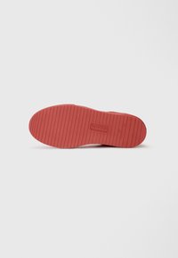 Sole di scarpa in gomma rossa con scanalature orizzontali e punta arrotondata, caratterizzata da un logo in rilievo al centro e una superficie liscia.