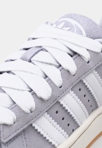 Light gray suede sneaker with white laces, featuring striped accents, perforations, and a textured, rubber outsole.