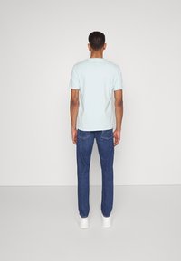 Camiseta de manga corta azul clara exhibida en una persona, combinada con jeans azul oscuro y zapatillas blancas, vista desde atrás.