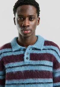 Sweter w paski w odcieniach niebieskiego, ciemnoniebieskiego i bordowego. Miękki, teksturowany dzianinowy sweter z kołnierzem i trzema czarnymi guzikami przy szyi.