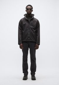 Chaqueta impermeable negra con cuello alto, cierre de cremallera y bolsillos laterales, combinada con pantalones negros y calzado negro resistente.