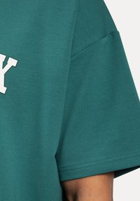 Turkusowa koszulka z luźnym krojem, krótkimi rękawami i białym nadrukiem litery "Y" na przodzie. Miękka w dotyku i z wyraźnymi detalami przeszycia.