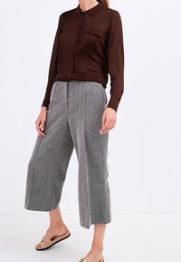 Brun langærmet skjorte med knaplukning og krave, parret med grå tweed bukser med bred ben og lysebrune sandaler med guld detaljer.