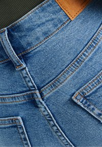 Blå denimjeans med ljus tvätt, synlig sömnad och en läderlapp. Midjan har en klassisk design och två bakfickor.