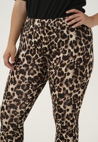 Leggings en imprimé léopard en marron et beige, présentant un design ajusté avec une texture lisse et une taille élastique pour le confort.