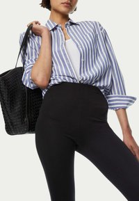 Niebiesko-biała w paski koszula zapinana na guziki, noszona na białej koszulce na ramiączkach, połączona z czarnymi legginsami w wysokim stanie i plecioną czarną torbą.
