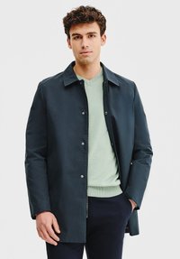 Granatowy płaszcz z kołnierzem, srebrnymi guzikami i długimi rękawami, noszony na jasnoszarym swetrze, na białym tle.