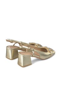 Złote metaliczne buty typu slingback z niskim obcasem w kształcie bloku. Posiadają akcent z cyrkonii z przodu oraz wycięcie na palce. Gładka tekstura.