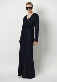 Mörkblå långärmad klänning med v-ringning, slät yta och lätt utställd nederdel. Har klockformade ärmavslut och subtila mönsterdetaljer.