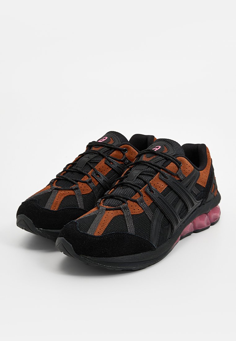 Scarpe da ginnastica nere e marroni con tomaia in rete, dettagli testurizzati e suola ammortizzata rosa. Presentano un design con lacci e materiali sintetici.