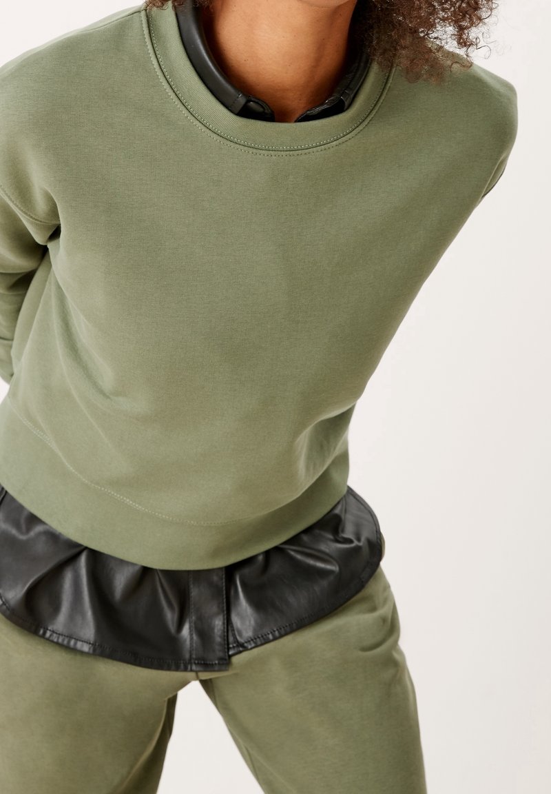 Felpa verde oliva chiaro con colletto a girocollo a coste e orlo peplum in finta pelle nera. Tessuto morbido con un fit rilassato.