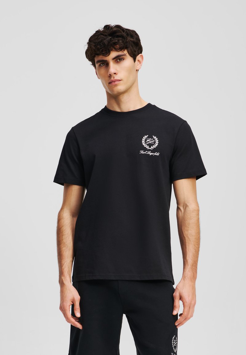 Svart bomull T-shirt med rund halsringning, kort ärm och en vit logotyp prydd med ett lagerbladsmotiv på bröstet.
