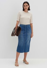 Haut ajusté beige à manches courtes associé à une jupe en denim bleu mi-longue avec des poches avant et une taille ajustée ; tenant un sac marron.